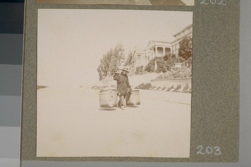 [Street scene. Chinese man carrying large containers.]