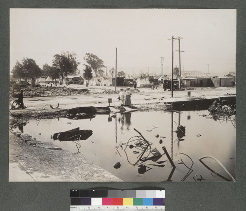 [Women at flooded lot. Refugee tents in background.]