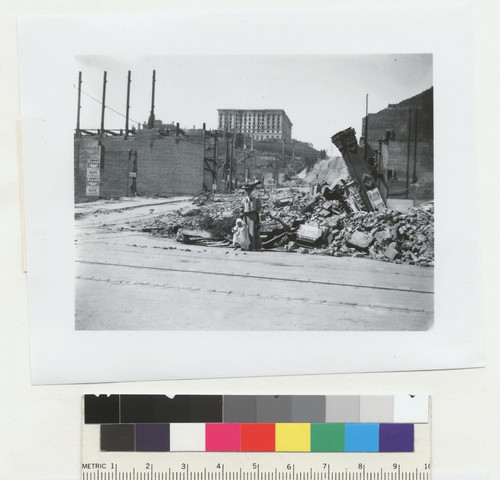 [Woman and child posing before ruined lot. Powell St., left; Fairmont Hotel atop Nob Hill in distance.]