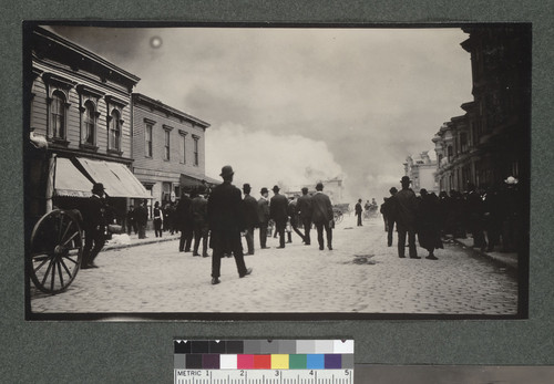 [Crowd gathered in unidentified street, watching fire in distance.]