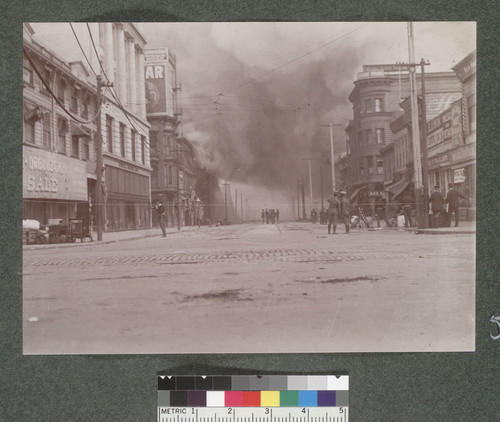 [Soldiers and police officers patrol Sixth St. near burning building.]