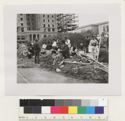 [Workers on break during street cleaning. Along Geary St. at Union Square. Hotel St. Francis in background.]