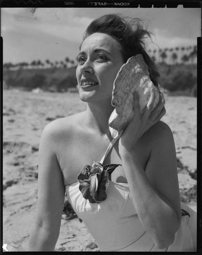 Betty Herrick [?] on beach with seashell, [1935-1955]