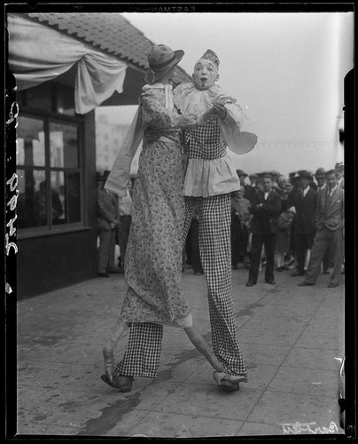 Clown on stilts dancing with tall puppet, advertising dance marathon, Santa Monica, 1928