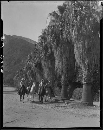 Cowboys riding horses on dirt road next to affluent residential property, Palm Springs