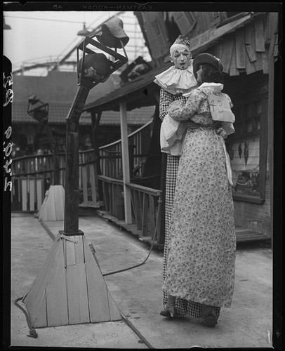 Clown on stilts dancing with tall puppet, advertising dance marathon, Santa Monica, 1928