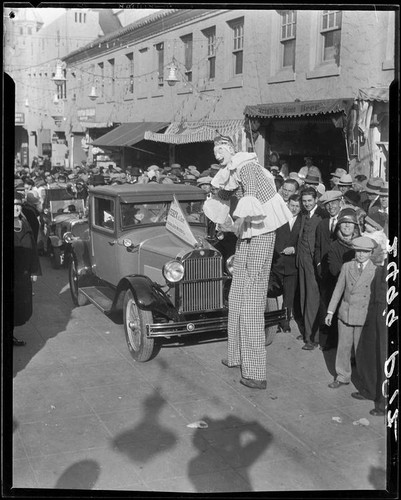 Clown on stilts, advertising dance marathon, with crowd and Essex car, Santa Monica, 1928