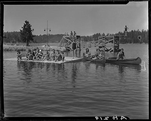 Young people in canoes, on floating dock, and on diving platforms, Lake Arrowhead, 1929