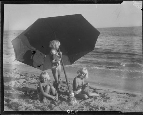 Mawby triplets with umbrella and dolls at beach, Malibu, 1928