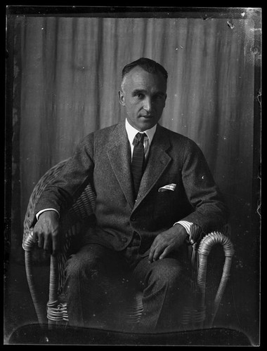 Portrait of Adelbert Bartlett, in suit and tie, seated in wicker chair ...