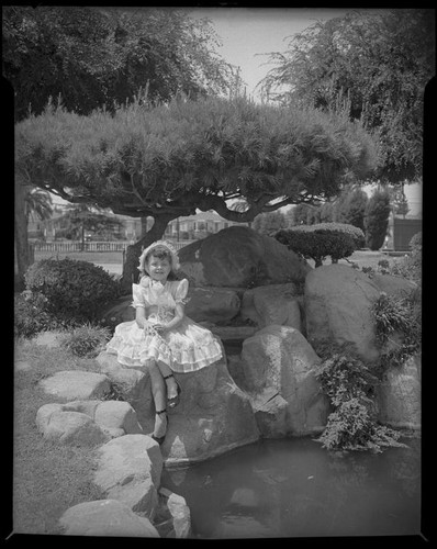 Helena Burnett in dress and bonnet sitting next to a pond, 1947-1950