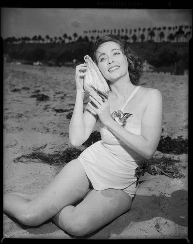 Betty Herrick [?] on beach with seashell, [1935-1955]