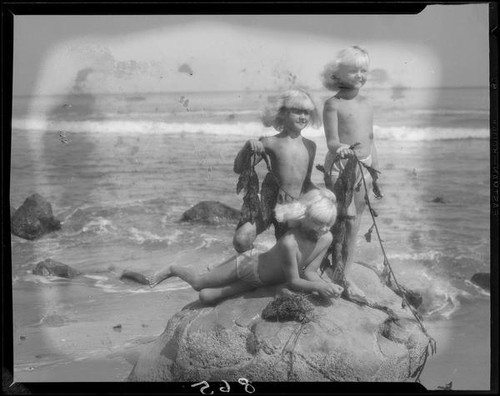 Mawby triplets on rock with seaweed at beach, Malibu, 1928