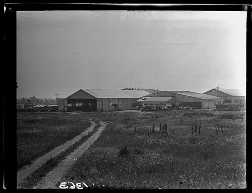 Field with tire tracks, cars, and buildings, [1920s?]