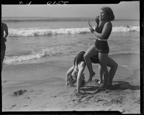 Young women at beach, performing back bend and applying makeup, Venice, 1930