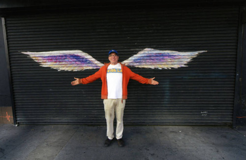 Unidentified man in a red jacket posing in front of a mural depicting angel wings