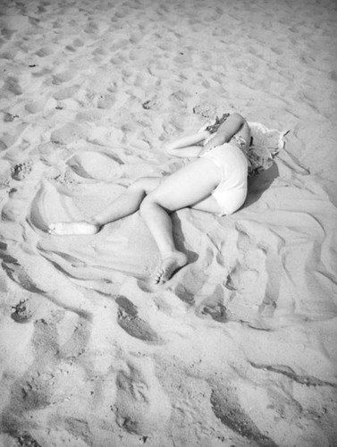 Young woman lying on the sand at the beach — Calisphere
