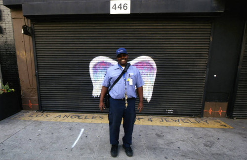 Unidentified man, possibly a Southern California Gas Company worker, posing in front of a mural depicting angel wings