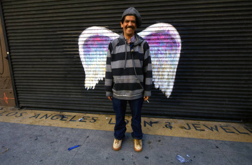 Unidentified man in striped hoodie posing in front of a mural depicting angel wings