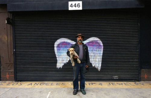 Unidentified man holding his dog and posing in front of a mural depicting angel wings