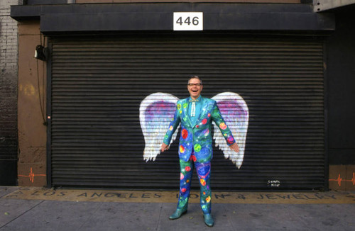 Charles Phoenix posing in front of a mural depicting angel wings