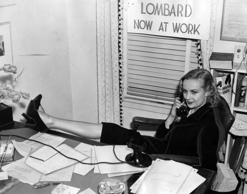 Carole Lombard, press agent, props feet on desk