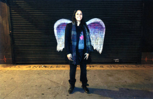 Unidentified woman with scarf posing in front of a mural depicting angel wings