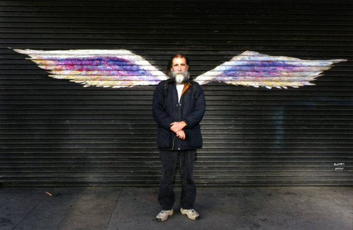 Unidentified man with facial hair posing in front of a mural depicting angel wings