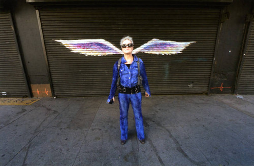 Unidentified woman in sunglasses posing in front of a mural depicting angel wings