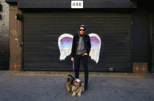 Unidentified man with two dogs posing in front of a mural depicting angel wings