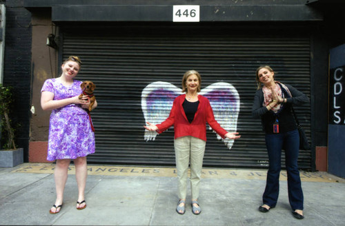 Katie Dunham, Louise Steinman, and an unidentified woman posing in front of a mural depicting angel wings