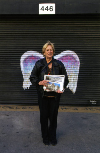 Unidentified woman holding a newspaper posing in front of a mural depicting angel wings