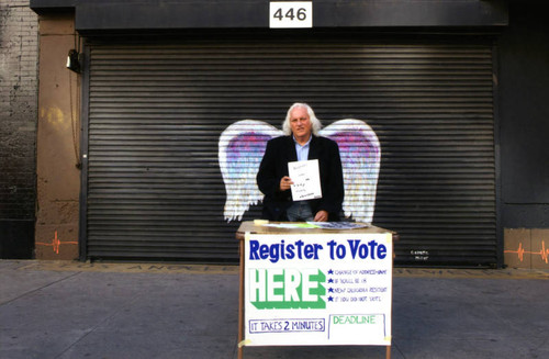 Unidentified man at a voter registration table posing in front of a mural depicting angel wings