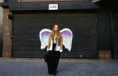 Unidentified woman posing in front of a mural depicting angel wings