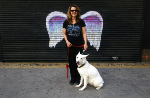 Unidentified woman and dog posing in front of a mural depicting angel wings