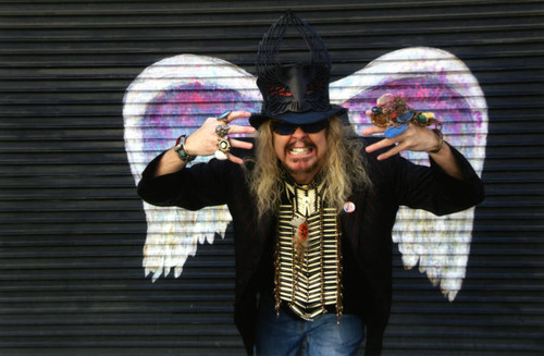 Unidentified man in costume and sunglasses posing in front of a mural depicting angel wings