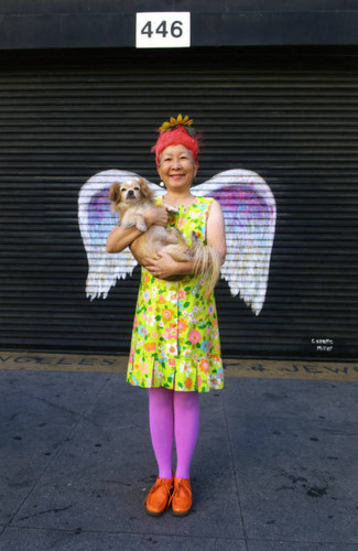 Amy Inouye holding a dog and posing in front of a mural depicting angel wings