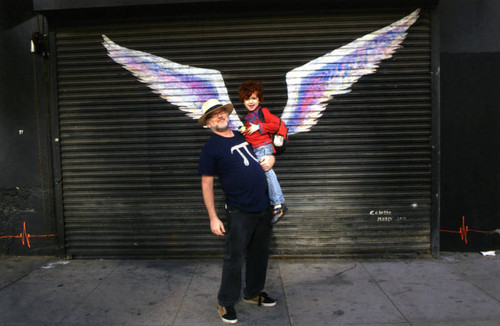 Unidentified man holding a child and posing in front of a mural depicting angel wings