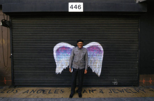 Unidentified man in a black cap posing in front of a mural depicting angel wings