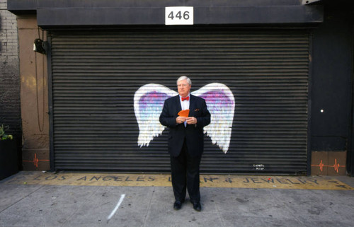 John Welborne posing in front of a mural depicting angel wings