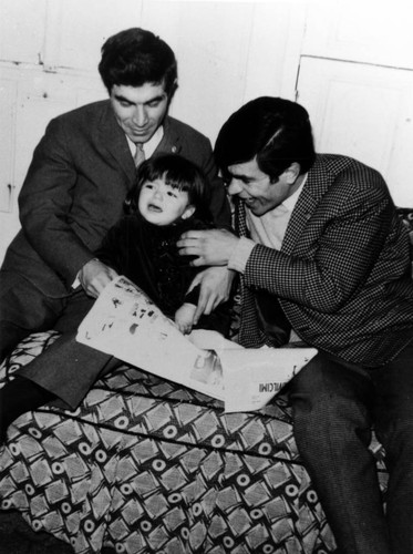 Toddler reads a newspaper with her uncle and father