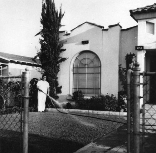 Mexican American man watering lawn in front of home