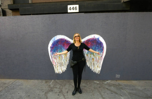 Unidentified woman in sunglasses posing in front of a mural depicting angel wings