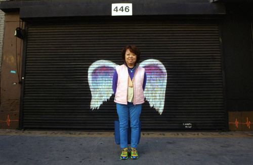 Unidentified woman in a pink vest posing in front of a mural depicting angel wings