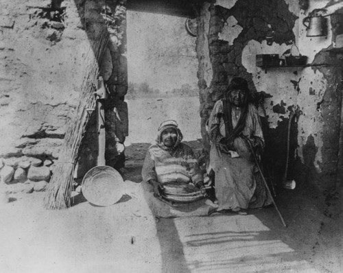 Native American women sitting by an adobe