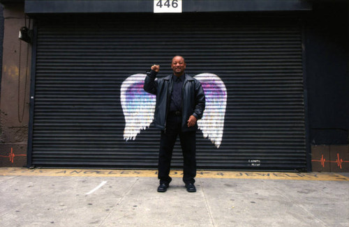 Unidentified man in a black leather jacket posing in front of a mural depicting angel wings