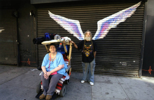 Unidentified man with woman in a wheelchair posing in front of a mural depicting angel wings