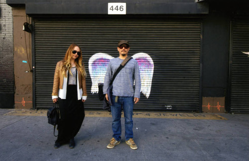 Unidentified man and woman posing in front of a mural depicting angel wings