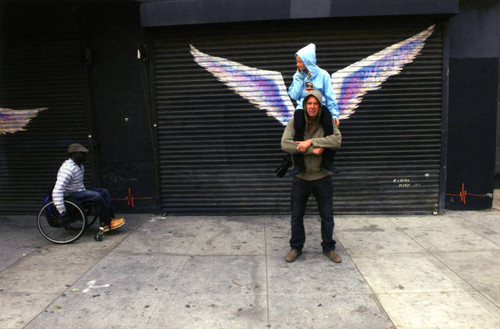 Unidentified man holding a child and posing in front of a mural depicting angel wings