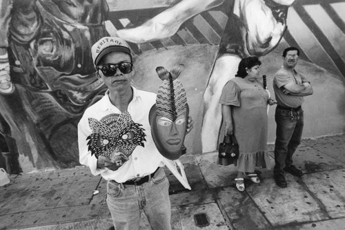 Man holding masks in front of mural, Echo Park